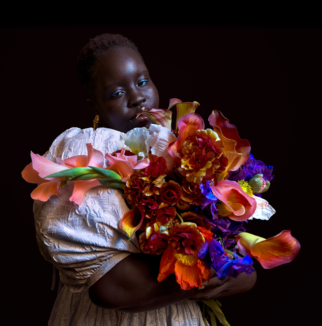 Foto em pouca luz de uma pessoa segurando um buquê de flores coloridas.